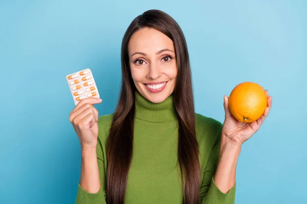 Foto av ganska glänsande ung kvinna bära gröna polotröja glasögon ler hålla medicin orange frukt isolerad blå färg bakgrund — Stockfoto