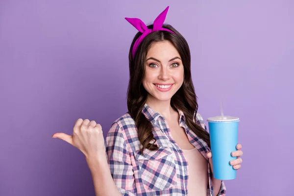 Fénykép portré mosolygós lány mutató hüvelykujj háta mögött kezében kék műanyag csésze egyik kezében elszigetelt élénk lila színű háttér — Stock Fotó