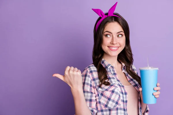笑顔の女性が親指を後ろに向ける姿を、真っ青な紫色の背景に孤立した片手にカップを持つ空白の空間 — ストック写真
