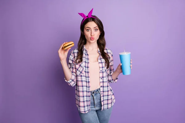 Foto retrato de una chica guapa comiendo hamburguesa bebiendo refrescos dulces enviando un beso de aire aislado sobre un fondo de color púrpura brillante — Foto de Stock