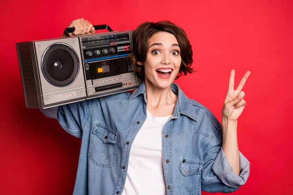 Foto de funky morena millennial senhora segurar boom box mostrar v-sign desgaste jeans camisa isolada no fundo de cor vermelha — Fotografia de Stock