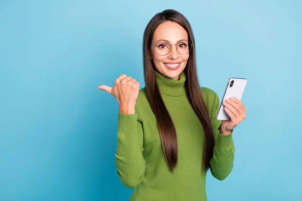 Foto von glänzenden süßen Dame gekleidet Rollkragenbrille hält moderne Gadget zeigt leeren Raum isoliert blaue Farbe Hintergrund — Stockfoto