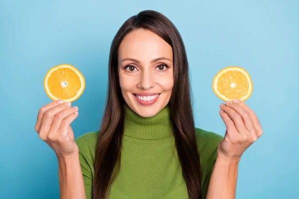 Foto de brillante encantadora joven mujer usar gafas de cuello alto verde sonriendo sosteniendo rodajas de fruta naranja aislado fondo de color azul —  Fotos de Stock