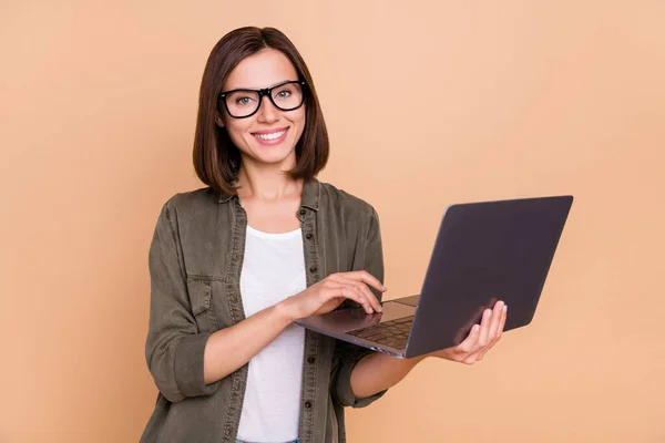 Фото веселой радостной леди держать ноутбук подготовить проект носить очки рубашки хаки изолированный бежевый цвет фона — стоковое фото