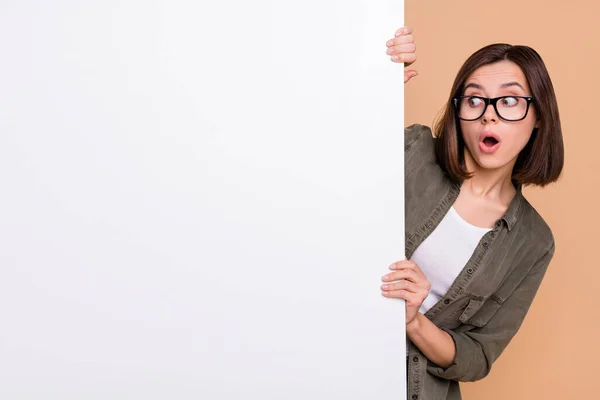 Фотографія допитливої шокованої жінки дивіться плакат інформацію носити специфікації сорочки хакі ізольовані бежевий колір фону — стокове фото