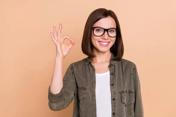 Фото надежной позитивной леди показать Оки знак одобрения сделки носить очки рубашки хаки изолированный бежевый цвет фона — стоковое фото