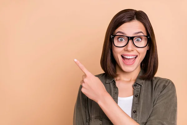 Photo of excited lady direct finger empty space open mouth wear specs khaki shirt isolated beige color background