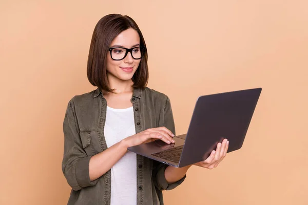 Photo of positive worker lady hold laptop wpisując smm aktualności nosić specyfikacje khaki koszula odizolowany beżowy kolor tło — Zdjęcie stockowe