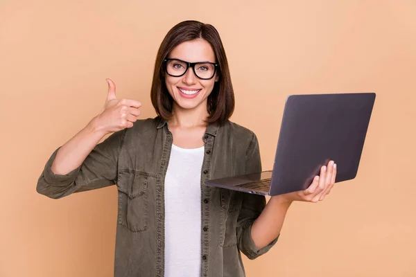 写真の信頼性の高い女性ホールドノートパソコンの上昇親指アップ着用アイウェアカーキシャツ孤立ベージュ色背景 — ストック写真