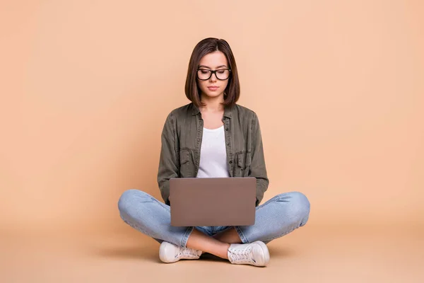 Fotografie soustředěná dáma sedět podlaha programování kód nosit brýle khaki košile izolované béžové barvy pozadí — Stock fotografie