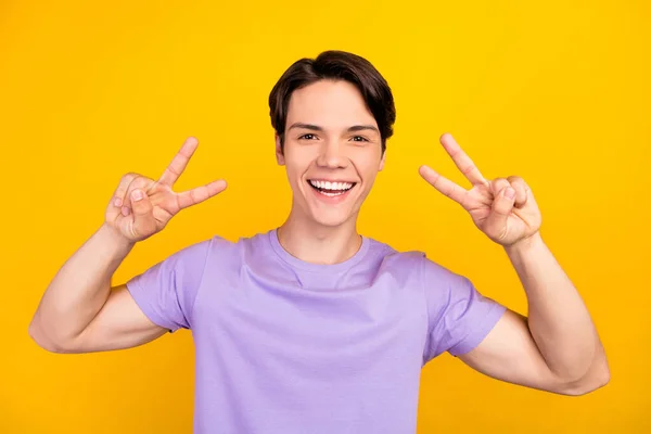 Foto von aufgeregten positiven Kerl zeigen zwei V-Zeichen Spaß haben tragen lila T-Shirt isoliert gelbe Farbe Hintergrund — Stockfoto