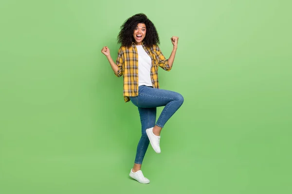 Plná velikost fotografie funky vlnitý účes mladá dáma ruce pěsti křičí nosit žluté košile džíny tenisky izolované na zeleném pozadí — Stock fotografie