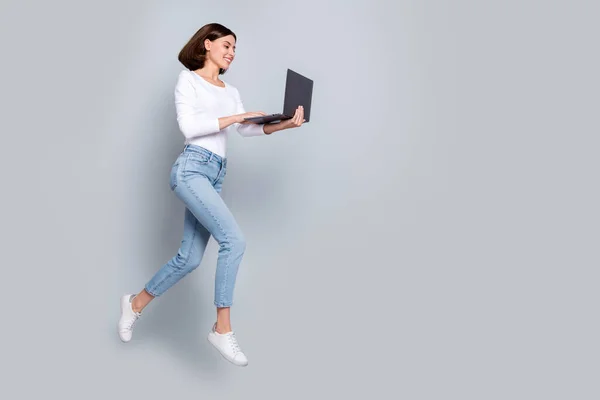 Fotografie rozkošná sladká mladá dáma oblečená bílé oblečení chatování moderní gadget prázdný prostor jumping vysoký izolované šedé barvy pozadí — Stock fotografie
