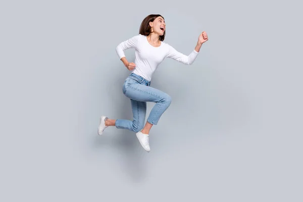 Foto de encantadora senhora bonita vestida roupas brancas sorrindo correndo rápido olhando espaço vazio saltando alto isolado fundo de cor cinza — Fotografia de Stock