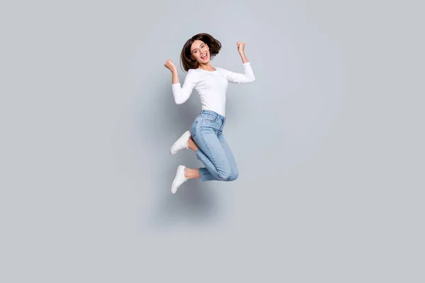 Foto de mujer joven afortunada impresionada usando traje blanco saltando puños altos sonriendo aislado fondo de color gris — Foto de Stock