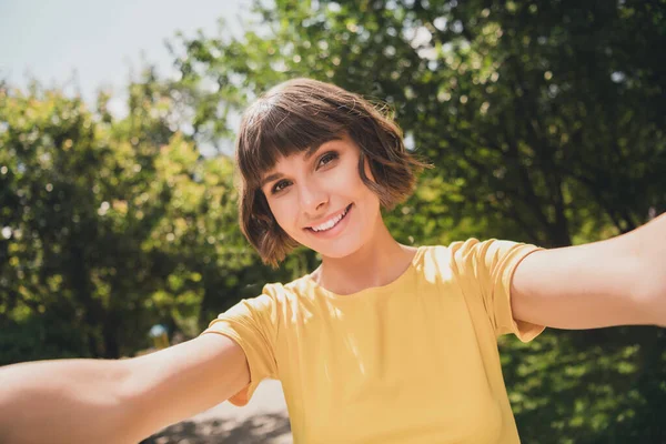Фото позитивной юной леди в желтых очках с футболками, идущей с селфи, улыбающейся на открытом воздухе городского парка — стоковое фото