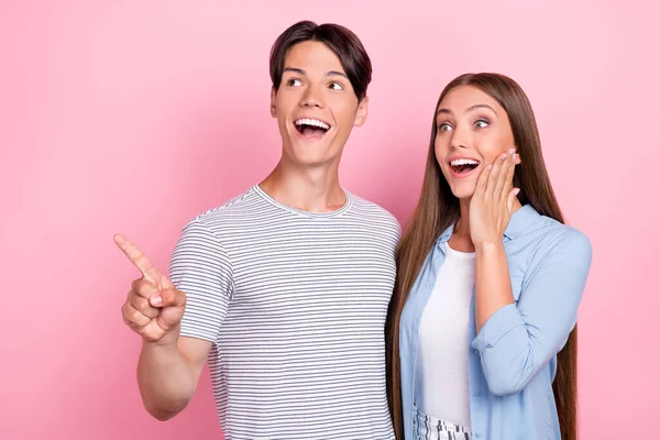 Foto de impressionado casal chocado usar roupas casuais apontando dedo saque espaço vazio braço bochecha isolado cor de fundo rosa — Fotografia de Stock