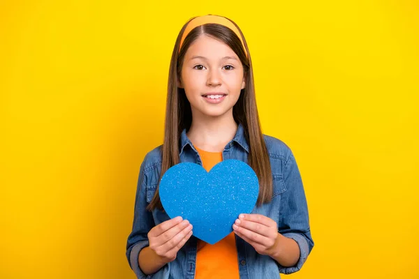 Foto de doce adorável menina pré-adolescente vestida camisa jeans segurando braços azul coração sorrindo isolado cor amarela fundo — Fotografia de Stock
