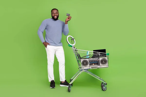 Foto de chico afro alegre usar jersey gris comprar tarjeta de crédito dispositivos modernos aislado fondo de color verde — Foto de Stock