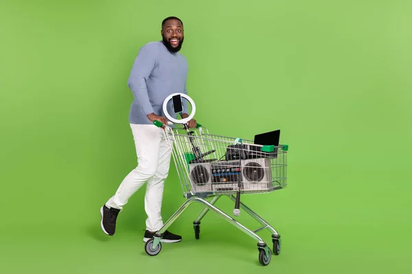 Fotografie šokované afro chlap nosit pullover chůze nákupní tác moderní zařízení izolované zelené barvy pozadí — Stock fotografie