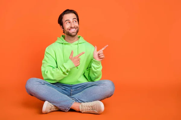 Full size photo of brunet young guy sit index promo wear green hoodie jeans shoes isolated on orange color hintergrund — Stockfoto