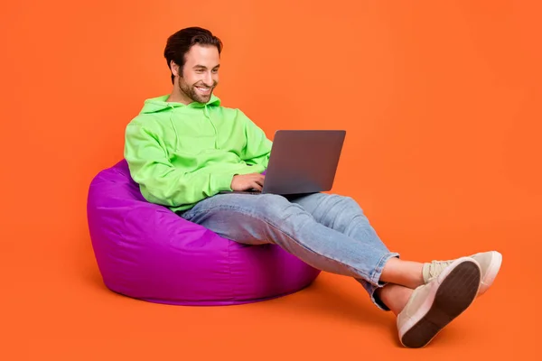 Pleine photo du corps de brunet jeune gars type ordinateur portable porter vert sport tissu jeans baskets isolées sur fond de couleur orange — Photo
