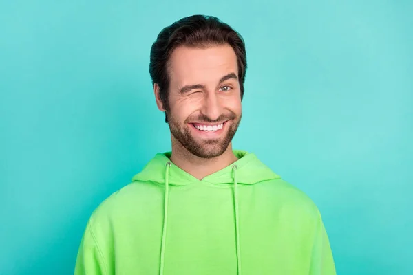Kuva hauska luotettava mies vinkki silmä kiiltävä hymy flirttailu kulumista vihreä huppari eristetty turkoosi väri tausta — kuvapankkivalokuva
