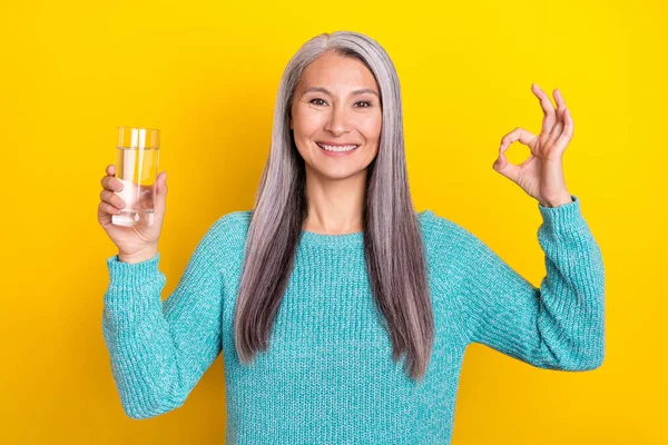 Ritratto di attraente allegra donna dai capelli grigi che tiene l'acqua mostrando ok-segno annuncio isolato su sfondo di colore giallo brillante — Foto Stock