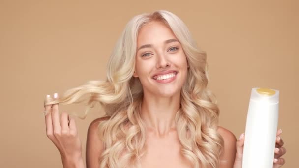 Pretty lady hold shampoo touch wavy hairdo isolated pastel color background — Stock Video