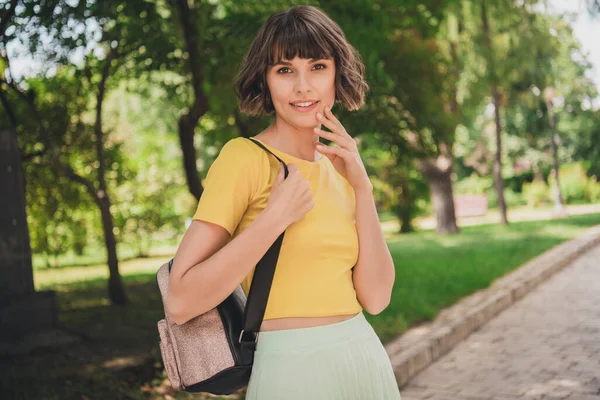 Фото очаровательной юной леди, одетой в желтую футболку рюкзак прогуливаясь улыбаясь на открытом воздухе городского парка — стоковое фото