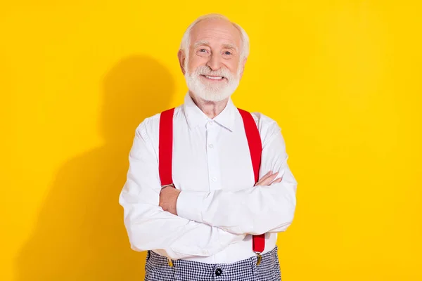 Foto de engraçado velho cinza cabelo homem cruzado braços desgaste branco camisa suspensórios isolados no fundo de cor amarela — Fotografia de Stock