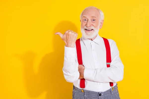 Fénykép a lenyűgözött idős szürke haj vicces ember pont üres tér kopás fehér ing nadrágtartó elszigetelt sárga színű háttér — Stock Fotó