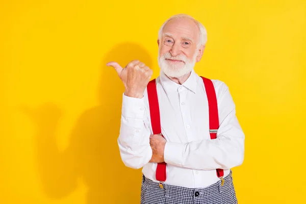 Fénykép a vicces öreg fehér haj férfi show hirdetés kopás fehér ing nadrágtartó elszigetelt sárga színű háttér — Stock Fotó