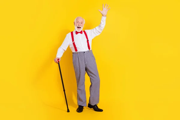 Foto de comprimento total do homem mais velho engraçado com vara desgaste gravata camisa branca suspensórios vermelhos calças quadriculadas sapatos isolados no fundo de cor amarela — Fotografia de Stock