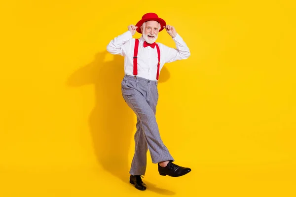 Foto de tamaño completo de divertido hombre viejo danza usar gorra roja corbata tirantes pantalones zapatos aislados sobre fondo amarillo —  Fotos de Stock