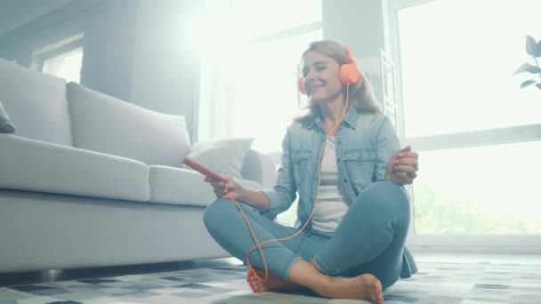 Señora despreocupada positiva sentarse piso sostener teléfono escuchar auriculares música — Vídeos de Stock