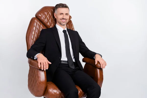 Foto van knappe zelfverzekerde volwassen broker gekleed zwart pak zitten gezellige lederen stoel glimlachen geïsoleerde grijze kleur achtergrond — Stockfoto