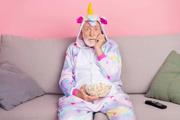 Foto von verängstigten Rentner Nachtwäsche insgesamt sitzend Couch beobachten beängstigend Film essen Popcorn isoliert rosa Hintergrund — Stockfoto