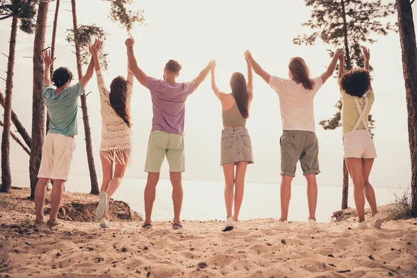 Vista trasera de la foto de los estudiantes amigos reuniendo costa levantar las manos usar ropa casual naturaleza verano playa —  Fotos de Stock