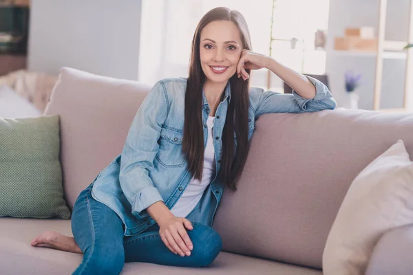 Ritratto di attraente donna dai capelli lunghi e allegra seduta sul divano che trascorre la giornata in armonia a casa al chiuso — Foto Stock