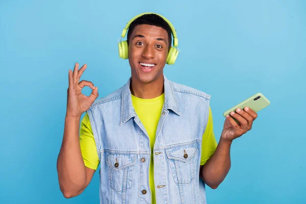 Foto de joven hombre afro alegre mostrar dedos símbolo okey uso de sonido perfecto smartphone aislado sobre fondo de color azul — Foto de Stock