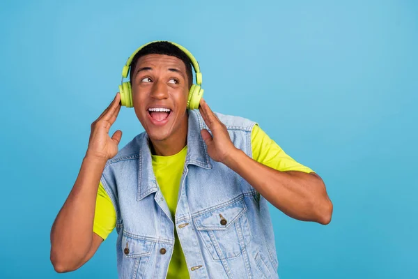 Foto de joven chico africano alegre mirada curiosa espacio vacío disfrutar de auriculares favoritos de la lista de reproducción aislados sobre fondo de color azul — Foto de Stock