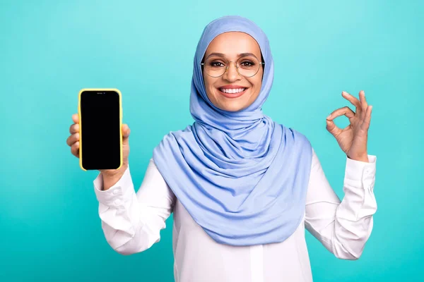 夢のような甘い若い女性の服を着たイスラムヒジャーブ眼鏡笑顔保持近代的なデバイス空のスペースキー隔離されたティール色の背景 — ストック写真