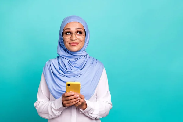 Foto de doce sonhador jovem senhora vestida islâmico hijab óculos sorrindo segurando moderno dispositivo vazio espaço isolado cor teal fundo — Fotografia de Stock