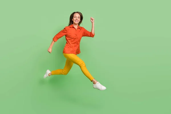 Foto di affascinante bella giovane donna indossare camicia rossa sorridente salto alto correre veloce spazio vuoto isolato colore verde sfondo — Foto Stock