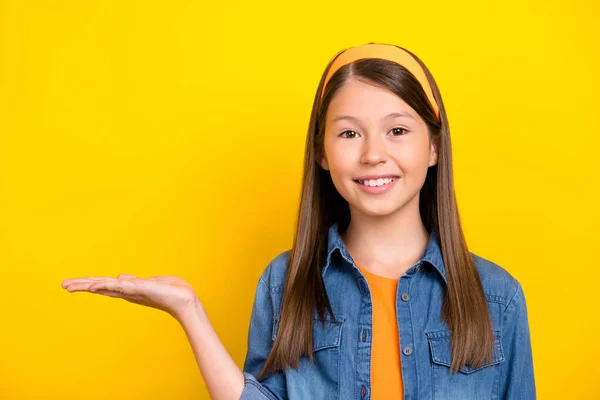 Foto de brillante linda estudiante niña usar camisa de mezclilla sonriente brazo de retención espacio vacío aislado color amarillo fondo —  Fotos de Stock