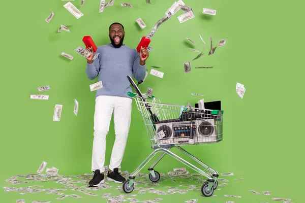 Fotografie funky africký chlap oblečený šedý svetr utrácení dolarů moderní gadgets izolované zelené barvy pozadí — Stock fotografie