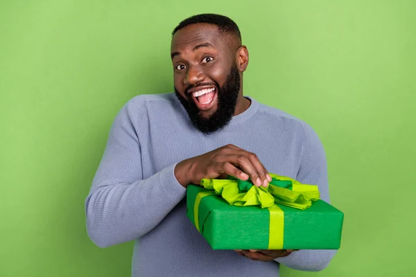 Fotografie legrační africký chlap oblečený šedý svetr s úsměvem otevření dárek balíček izolované zelené pozadí — Stock fotografie