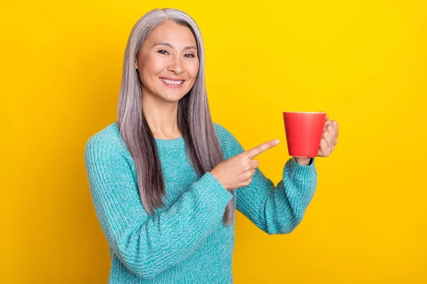 Портрет привабливої весело-сірої жінки, що п'є, показуючи трав'яний чай ізольований на яскраво-жовтому кольоровому фоні — стокове фото