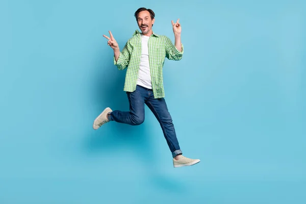 Повнорозмірний вигляд тіла привабливого веселого смішного чоловіка, який стрибає з v-знаком ізольовано на яскраво-синьому кольоровому фоні — стокове фото